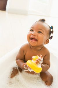 an African American baby girl in a bubble bath, holding a rubber ducky