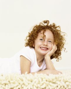 a little girl with red, curly hair posing on the carpet