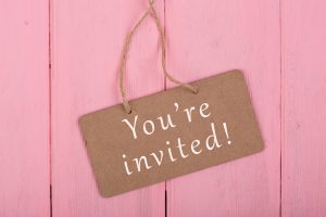 a gift tag reading, "you're invited' on a pink wooden background