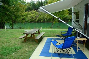 the canopy of an RV with chairs and a picnic table by a lake