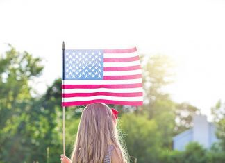 a photo taken of the back of a young girl as she stands in a field, holding the American flag