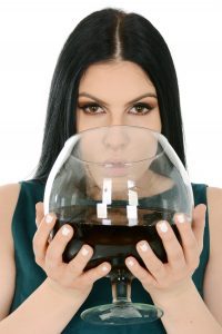 a close up of a brunette woman in a green dress drinking from a giant wine glass