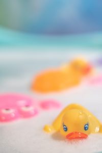 A close up of bath water with a rubber duck and some other toys floating in the bubbles