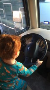 a toddler with auburn hair holding the steering wheel while pretending to drive