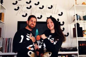 a dad, mom, and baby all wearing black Halloween pajamas with skeletons on them