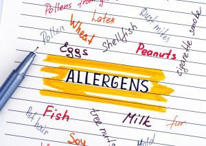 a sheet of lined paper with random food allergens written in different colors and fonts with the word ALLERGENS bold and highlighted in the middle