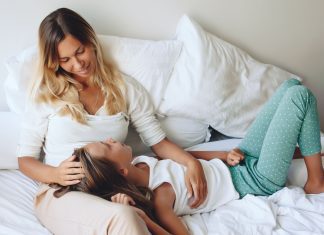 a daughter laying with her head in her mom's lap as the mom sits propped up in bed