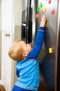 a toddler playing with alphabet magnets on the refrigerator