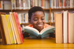 an African American boy smiling as he reads a book in the library
