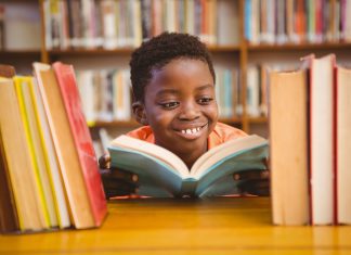 an African American boy smiling as he reads a book in the library