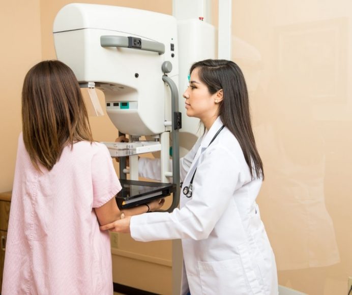 a woman in a pink gown getting help at her mammogram from a doctor in a white lab coat