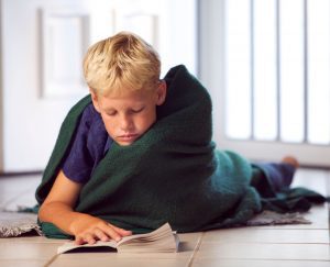 a boy wrapped in a blanket as he lays on the floor reading