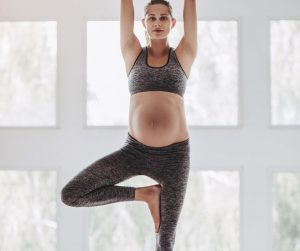 a pregnant woman doing yoga poses in front of a wall of windows