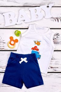 a baby boy's outfit of navy shorts and a white sleeveless onesie on a whitewashed background with a pacifier and the word BABY in white wooden letters
