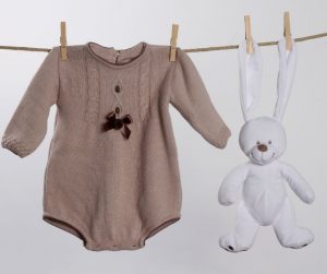 a knitted tan baby girl long sleeved onesie on a clothesline next to a bunny hanging from the clothesline by his ears