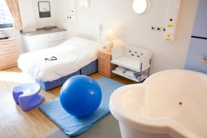 an empty birthing room with a tub and a yoga ball next to an empty bed