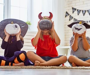 children in costumes sitting criss cross on the floor, holding halloween painted pumpkins in front of their faces