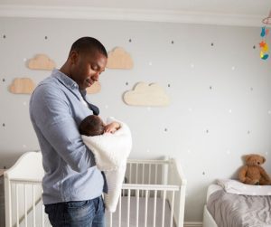 a dad standing in a nursery, holding his newborn son