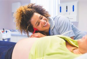 a doula listening to a pregnant mom's stomach to hear the baby's heartbeat