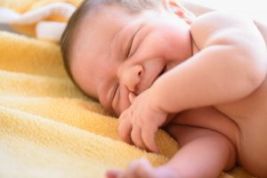 a newborn baby curled up on his side on a yellow blanket