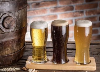 three glasses of foamy craft beer on a wooden plank next to a barrel