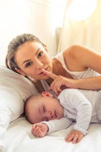 a mom with a finger to her lips shushing as her baby sleeps next to her