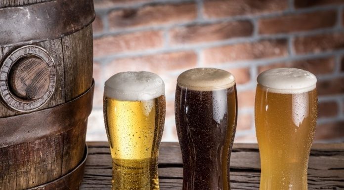 three glasses of foamy craft beer on a wooden plank next to a barrel
