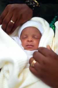 an African American baby swaddled in a blanket with both his mothers and his fathers hands next to him
