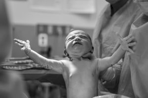 a newborn baby with his arms outstretched being held up by a midwife
