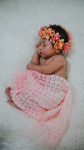 a newborn baby girl swathed in a pink blanket with a crown of flowers on her head