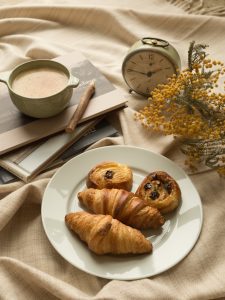 French croissants and pastries with cafe au lait on a table with flowers and an alarm clock
