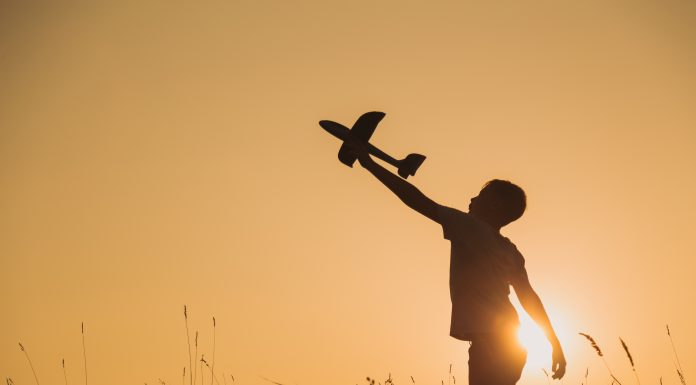 the silhouette of a boy with a toy airplane raised high as the sun sets behind him