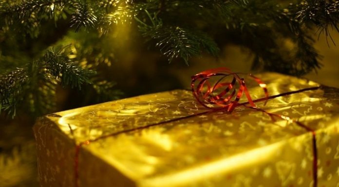 a box wrapped in golden paper with a red bow near the Christmas tree