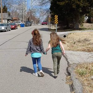 Two neighbor girls, from behind as they hold hands and walk down the street together