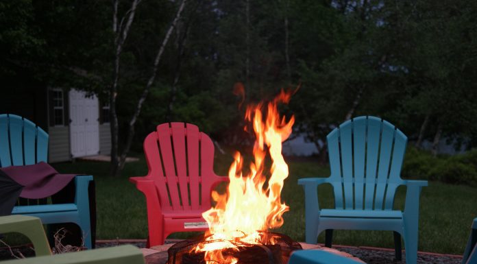 a roaring fire in a fire pit surrounded by empty, multicolored Adirondack chairs
