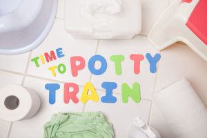 foam letters spelling "time to potty train" on a white tile floor with toilet paper, wipes, and a potty seat