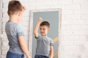 a young boy flexing his muscle as he looks into a mirror