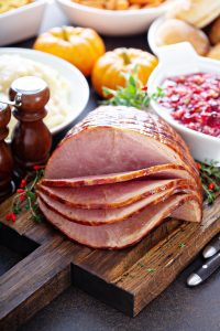 a spiral cut ham on a cutting board with Thanksgiving side dishes in the background