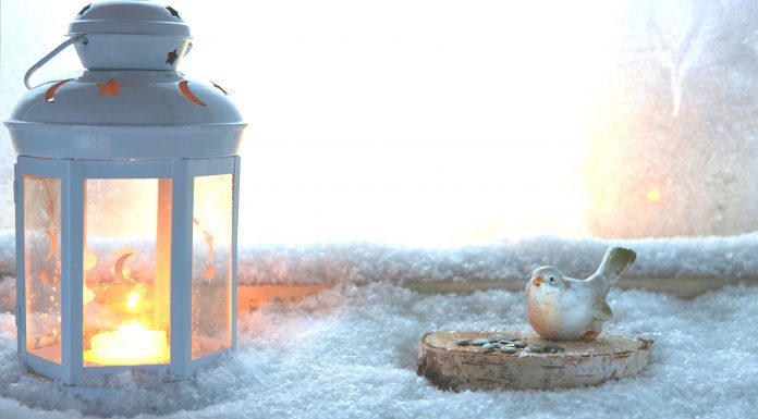 a white lantern lit on a snowy window ledge next to a ceramic bird and nest