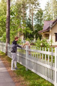 neighbors, a man and a woman, meeting over a white picket fence