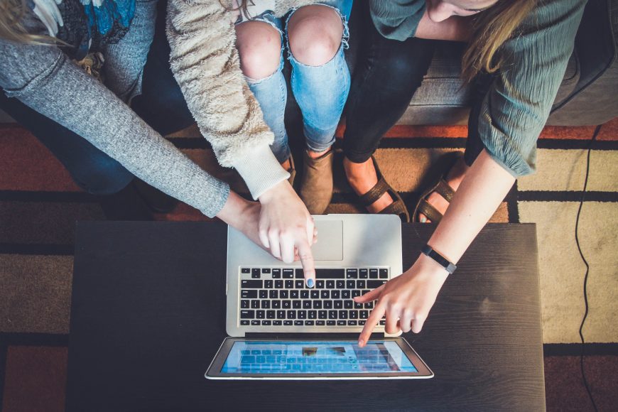 a close up of three people sitting next to each other on a couch as they each reach toward a laptop on the coffee table to work on college planning