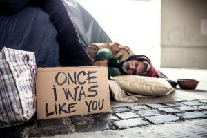a homeless man asleep on the street with a sign saying, "once, I was like you."