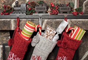 a close up of three stockings hanging on a stone mantle, filled with gifts from Santa