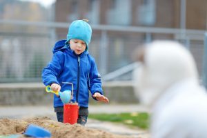 a boy bundled up In a coat as he plays in a sandbox outside