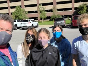 a mom and dad with their three kids, all wearing masks in a parking lot