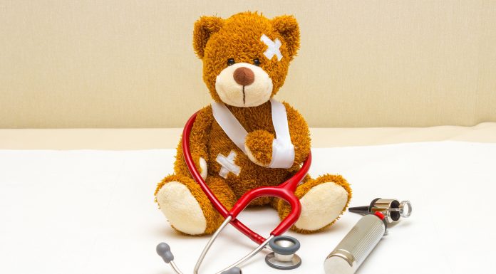 a teddy bear in a sling with bandages sitting on a doctor's table with a stethoscope