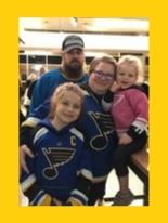 a mom, dad, and two little girls wearing St. Louis Blues hockey jerseys as they pose for a picture