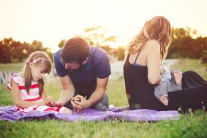 a family on a picnic blanket in the grass as the mom breastfeeds her baby