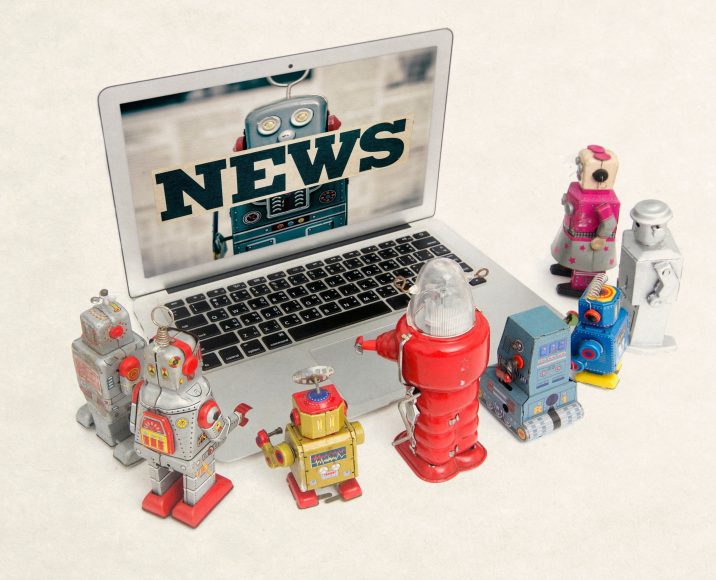 vintage robot toys gathered around laptop watching the news