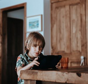 a child with medium length blonde hair sitting at a table while playing on a tablet during screen time